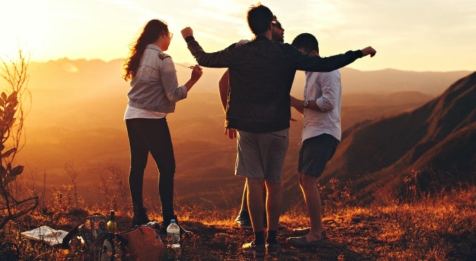Image of 4 people dancing on a sunset coloured mountain. In the background you can see yellow and orange coloured sunlight over the mountain side.